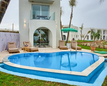 Luxury villa with heart-shaped swimming pool, lounge chairs, and palm trees at a tropical resort.