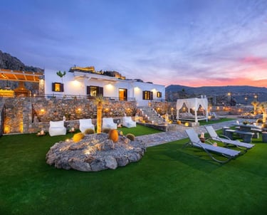 Luxury villa in Rhodes with lit patio, lawn seating, and sunset mountain views.