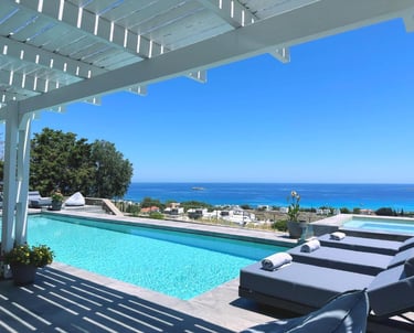 Luxury infinity pool with sun loungers overlooking the blue Mediterranean sea under a white pergola.