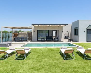 Luxury villa with a private swimming pool, sun loungers on a green lawn, and an outdoor dining area.