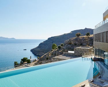 Luxury infinity pool at a coastal resort overlooking the Aegean Sea and rocky cliffs.
