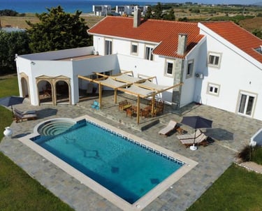Luxury white villa with red tile roof featuring a private swimming pool, patio, and ocean view.