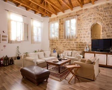 Rustic living room with exposed stone walls, wooden ceiling beams, and comfortable white sofas.