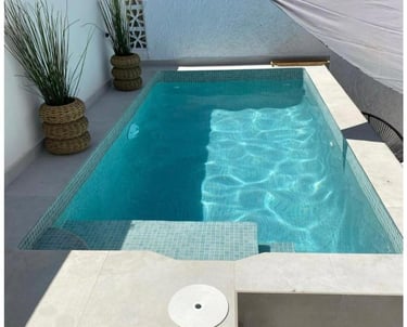 Small backyard swimming pool with blue mosaic tiles, poolside plants, and a sun shade sail.