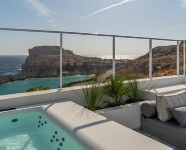 Luxury terrace with outdoor hot tub and lounge seating overlooking the turquoise sea and rocky coast.