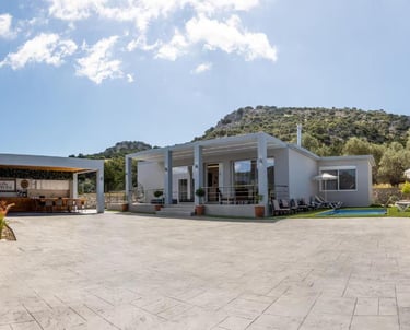 Luxury modern villa with private pool, outdoor kitchen, and mountain views under a sunny sky.