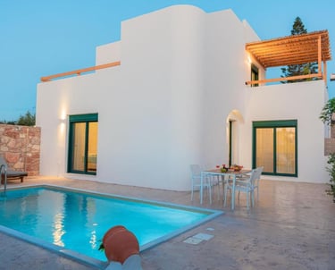 Luxury white villa with a private swimming pool and patio dining area at dusk.