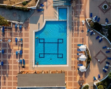 Aerial view of a luxury hotel swimming pool with blue lounge chairs and sun umbrellas on a tiled patio.