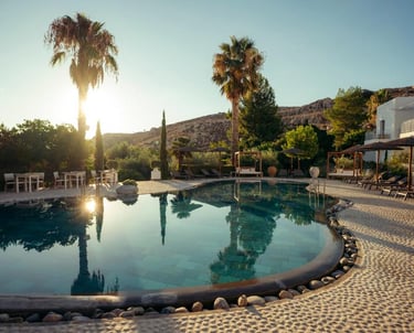 Luxury outdoor swimming pool at a Mediterranean resort with palm trees and lounge chairs at sunset.