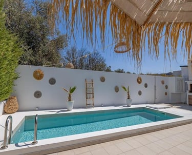 Luxury villa terrace with a private swimming pool, white walls, and bohemian style decor under a clear blue sky.