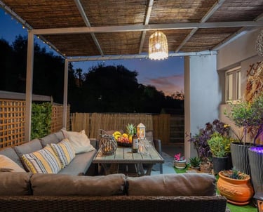 Cozy outdoor patio at dusk with a sectional sofa, rattan lighting, and garden decor.