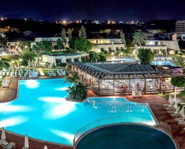 Night view of a luxury beachfront resort with illuminated swimming pools and lounge areas.