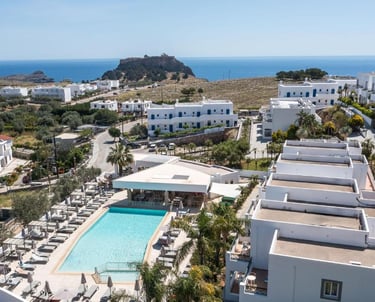 Aerial view of a luxury Greek island resort with a blue swimming pool and white villas near the sea.