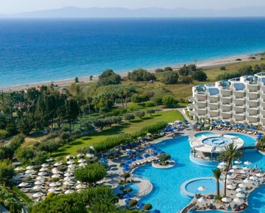 Luxury beach resort with blue swimming pools, sun loungers, and ocean views in Greece.