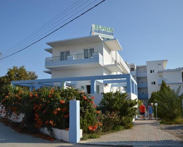 Exterior view of Elpida Beach Studios hotel in Greece with white architecture and blooming flowers.