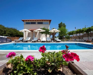 Luxury vacation villa with private swimming pool, sun loungers, and umbrellas under a clear blue sky.