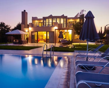 Luxury modern villa with a lighted swimming pool and lounge chairs at sunset.
