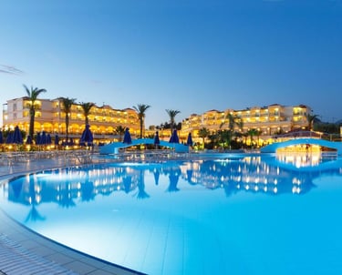 Luxury resort swimming pool with illuminated hotel buildings and palm trees at dusk.