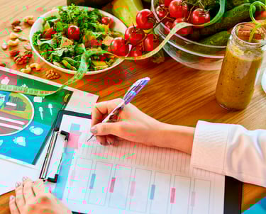 Mãos de nutricionista escrevendo em um prontuário sobre uma mesa com alimentos saudáveis