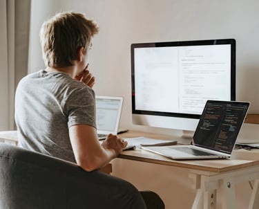 Un homme assis à un bureau avec deux ordinateurs portables et un iMac devant lui