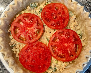 Freshly sliced red tomatoes layered on top of a savory pie filling in a fluted pastry crust.