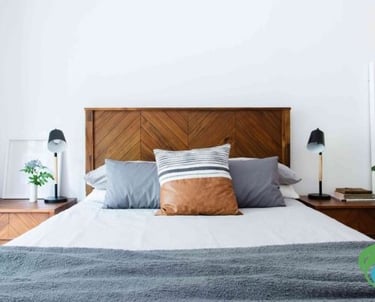 lit avec 3 oreillers, 1 drap blanc et un plaid gris foncé, avec deux commodes en bois vernis et la tête de lit également