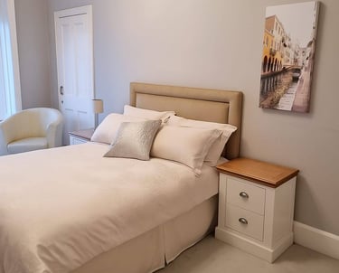 Neutral modern bedroom with a beige upholstered headboard, white bedding, and a Venice canal wall art piece.