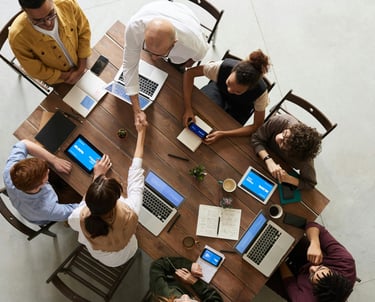 a group of people sitting around a table with laptops