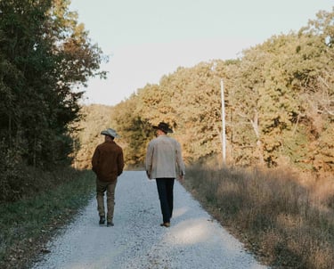 two men in cowboy hats and boots walking away down gravel road