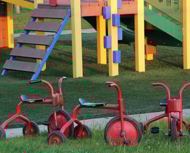 Colorful pieces of a playground for kids with 3 little red tricycle bikes parked in the foreground.