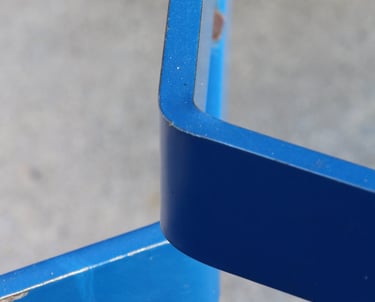 Two bright blue metal elements resembling hockey sticks set against blurry background..