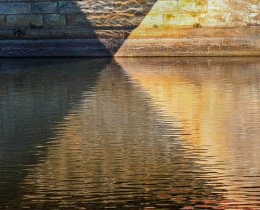 Riverbank casting beautiful multicolor geometric shadows on the water surface & wall.