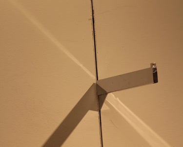 A beige wall with a protruding shelve bracket casting multiple shadows.