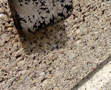 Bulky steel bent bracket, stripped off black paint, holding porous concrete edge.