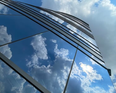 Looking up into the blue cloudy sky through reflection in a glass-steel building.