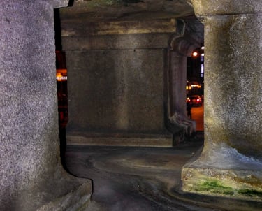Inside of the stone sculpture base with pillars and glimpses into a street life at night.