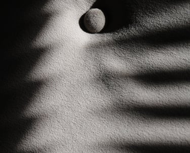 Monochrome image of shadows visible on a piece grayish fabric with a rounded button. 