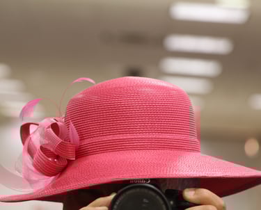 Male figure holding a photo camera and wearing red women's straw hat.