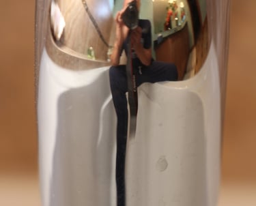  An image showing a mirror reflection of a male figure sitting with a camera on a white tub.