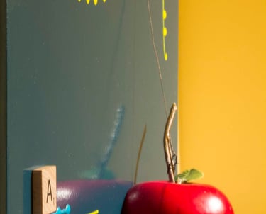 Red apple attached to dark green shiny surface with colorful marks & wooden letter A. 