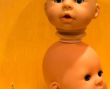 Small paper origami crane sitting next to 2 baby doll heads set on top of each other.