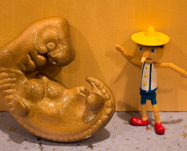 Still life with a plastic golden embryo next to a plastic toy figure of a Pinocchio. .