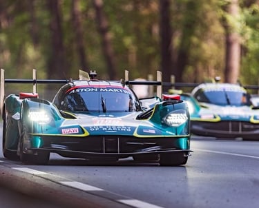 Aston Martin Valkyrie AMR Pro hypercars racing on a track through a forest at sunset.