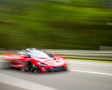 Motion blur of a red supercar speeding on Nurburging track with green forest background.