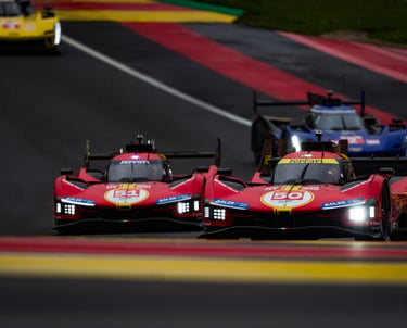 Ferrari 499P Hypercars racing on a track during an endurance motorsport event with headlights on.
