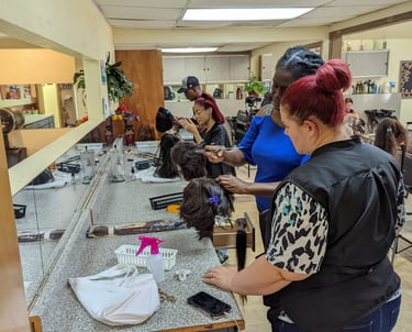 Students and instructors practice hair styling and cutting techniques on mannequin heads in a cosmetology school salon class.