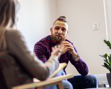 A young man with a beard facing a women in a therapy session