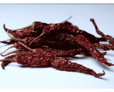 Close-up of dried red chilies placed on a white surface.