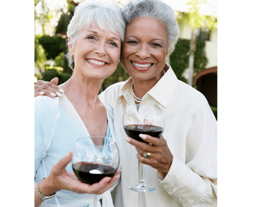 two lovely older women smiling and holding glasses of red wine