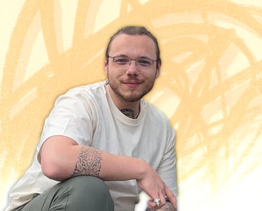 Smiling man with glasses and arm tattoos posing against an artistic yellow abstract background.
